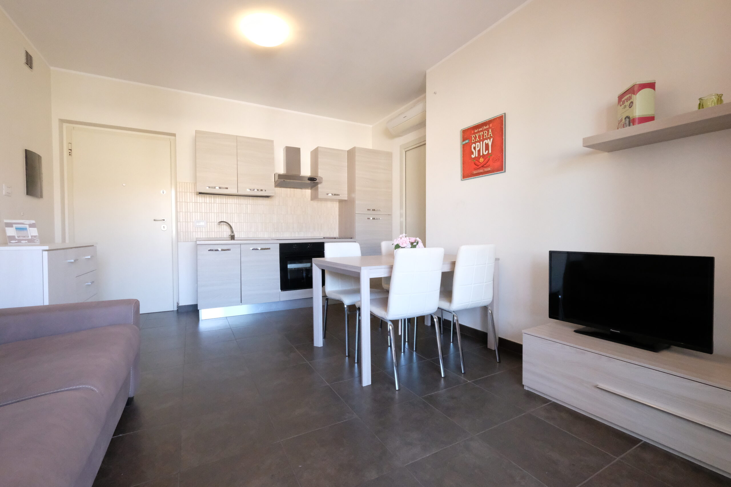 Sala e cucina con tavolo e sedie bianche ed una televisione Appartamento Pineto Vacanza Residence Claudia int. M
