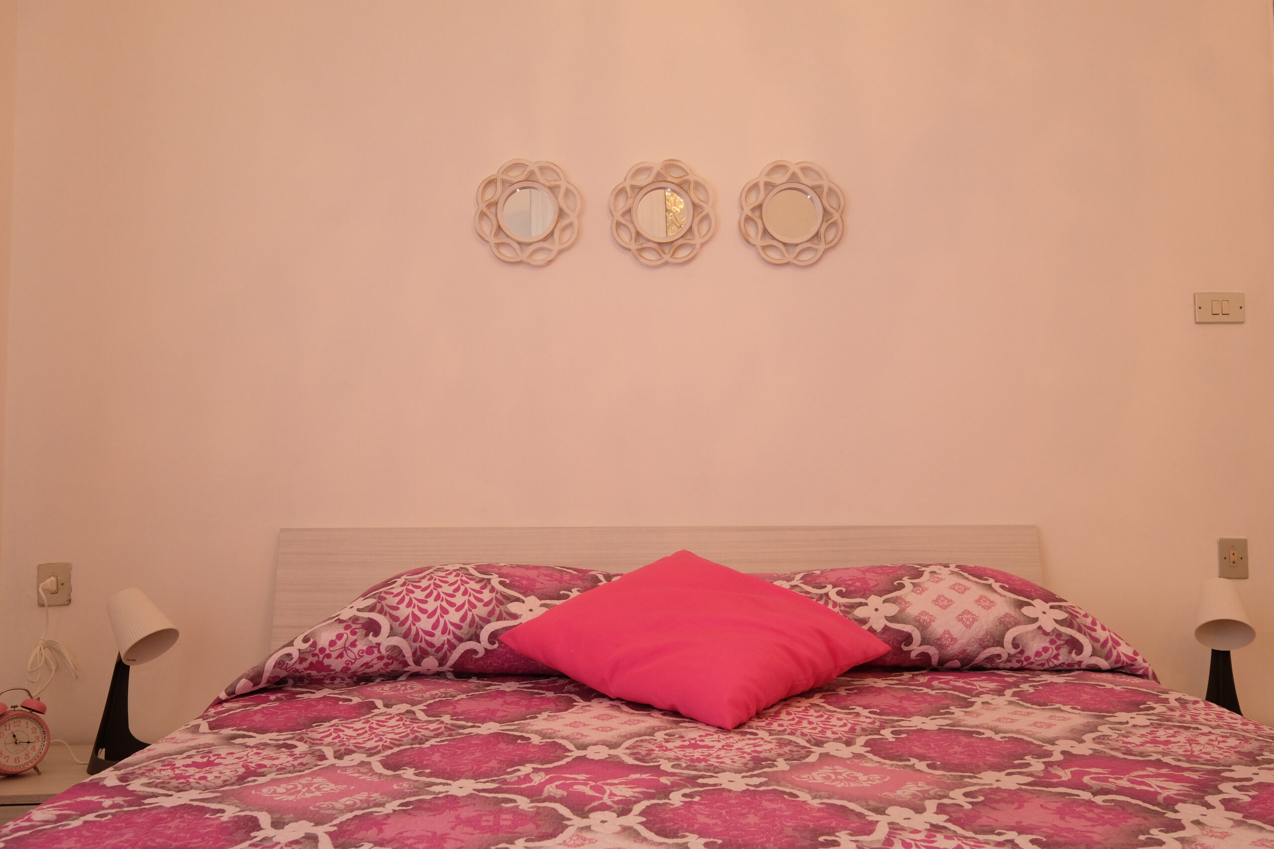 Camera matrimoniale con coperte rosa, un cuscino fucsia, due abat jour e la sveglia Appartamento Pineto Vacanza Orchidea PT