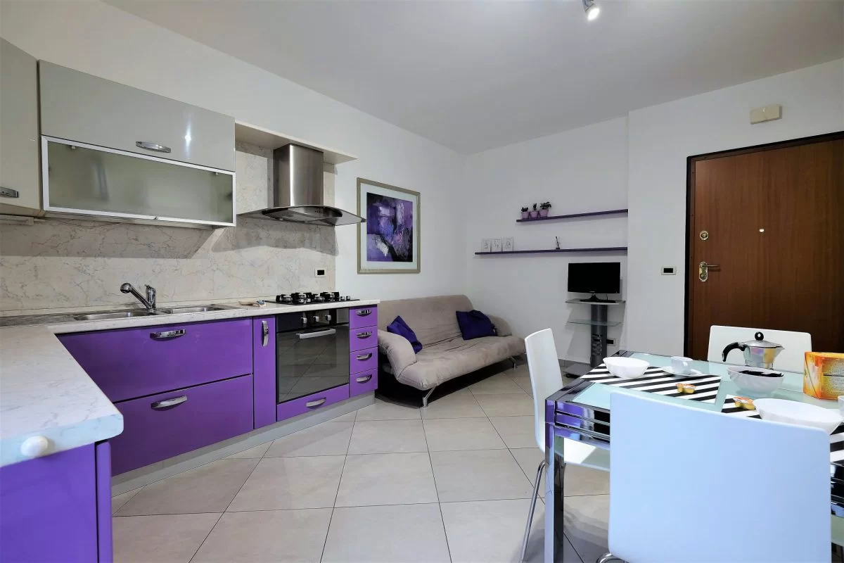 Cucina bianca e viola con sofà grigio e tavolo con sedie Appartamento Pineto Vacanza Mango