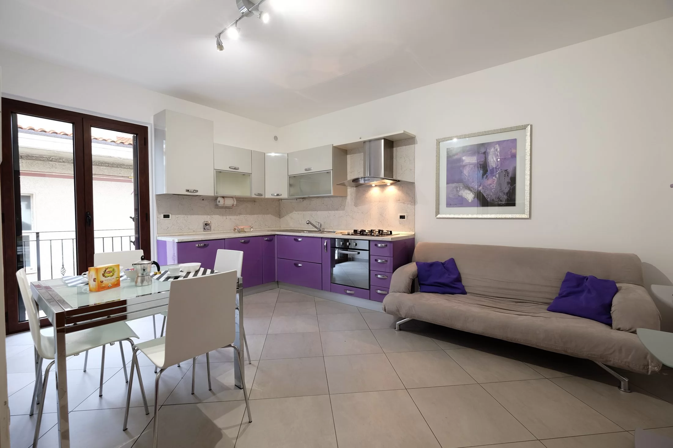 Sala e cucina viola con sofà grigio e tavolo e sedie Appartamento Pineto Vacanza Mango