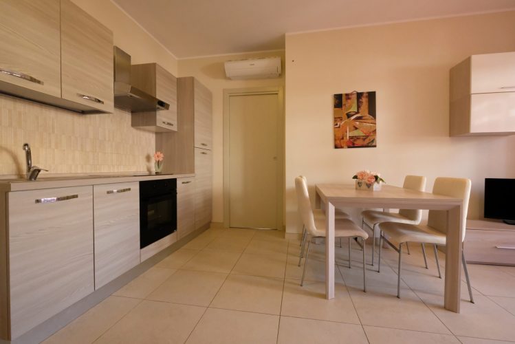 Cucina beige, aria condizionata e tavolo con sedie bianche Appartamento Pineto Vacanza Residence Claudia int. F