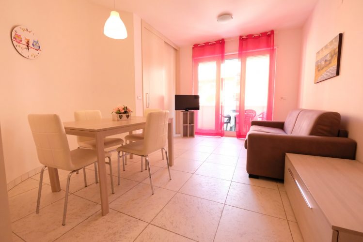Sala con divano rosso, credenza beige e tavolo con sedie bianche Appartamento Pineto Vacanza Residence Claudia int. I