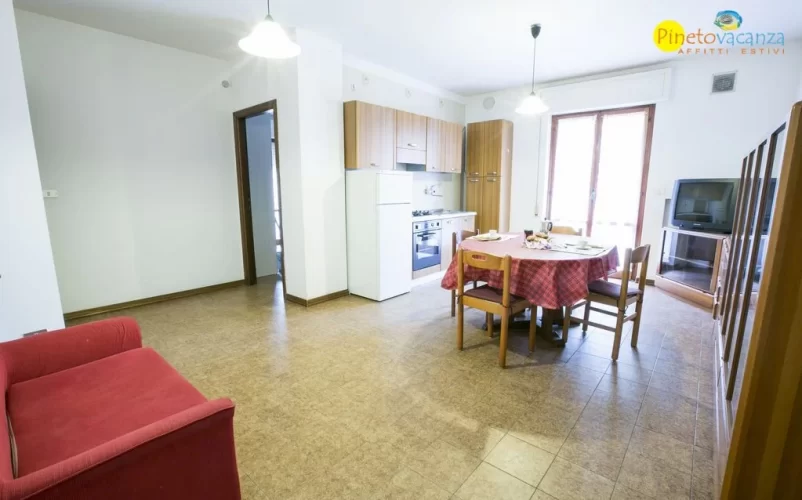 Cucina e sala con sofà rosso e tavolo e sedie in legno Appartamento Pineto Vacanza Gemma 4